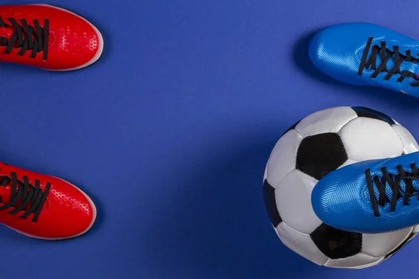 Top view of soccer ball and two pairs of soccer football sports shoes on blue background