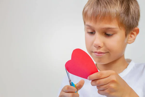 Coração de papel vermelho em mãos de crianças. Criança cortando coração de papel vermelho com tesoura — Fotografia de Stock