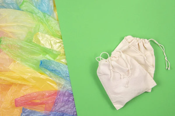 Many multicolored plastic bags with one eco natural reusable bag for shopping on green background. Zero waste, eco friendly, sustainability lifestyle, no plastic concept — Stock Photo, Image