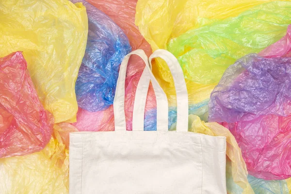 Many multicolored plastic bags with one eco natural reusable shopping bag background. Zero waste, eco friendly, sustainability lifestyle, no plastic concept