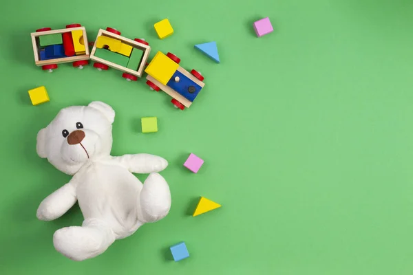 Bebê crianças brinquedos fundo. Urso de pelúcia branco, trem de brinquedo de madeira e blocos coloridos no fundo verde. Vista superior, flat lay — Fotografia de Stock