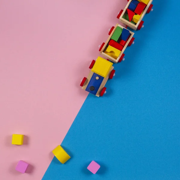 Fondo de juguete. Tren de juguete de madera con cubos de colores sobre fondo rosa y azul — Foto de Stock