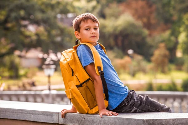 Niño con mochila sentado al aire libre y mirando a la cámara — Foto de Stock