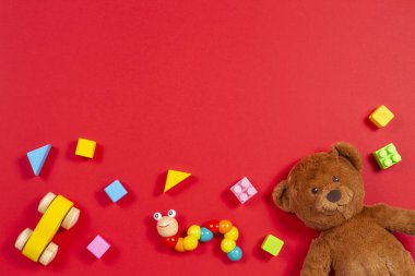 Baby kids toys background. Teddy bear, wooden car, colorful bricks on red background clipart