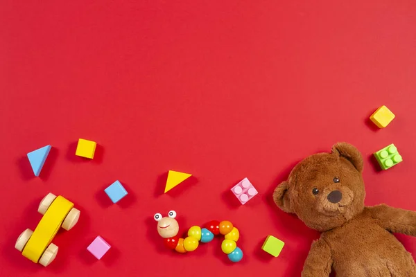 Dítě děti hračky pozadí. Medvídek, dřevěné auto, barevné kostky na červeném pozadí — Stock fotografie