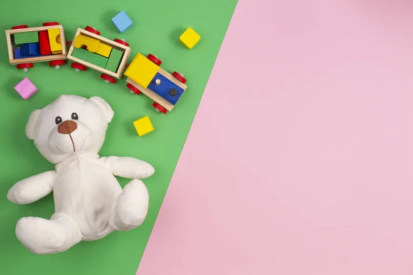 Bambino bambini giocattoli sfondo. Orsacchiotto bianco, treno giocattolo in legno e blocchi colorati su sfondo rosa e verde — Foto Stock