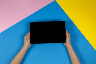 Tablet bilgisayarda mavi pembe ve sarı arka plan ile çocuk el