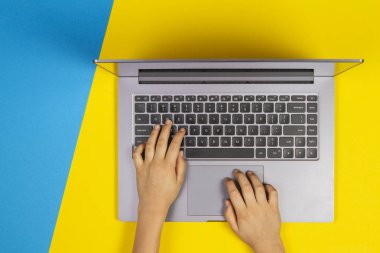 Tipik dizüstü bilgisayar klavye, üstten görünüm, sarı ve mavi arka plan üzerinde çocuk eller