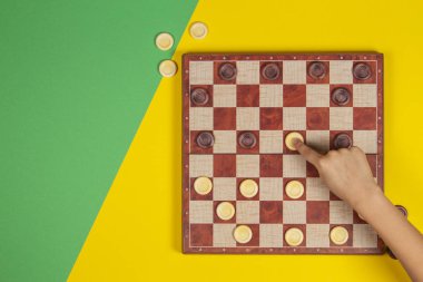 Çocuk el dama ekose desenli masa oyunu sarı ve yeşil arka plan üzerinde üstten görünüm oynamak.