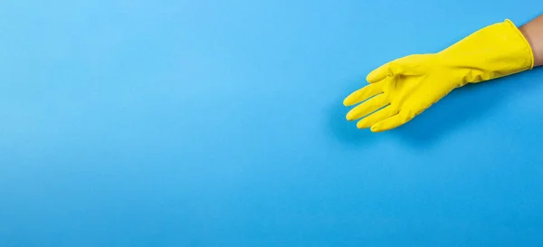Jedna kobieta ręka w żółtej gumowej rękawicy na niebieskim tle — Zdjęcie stockowe