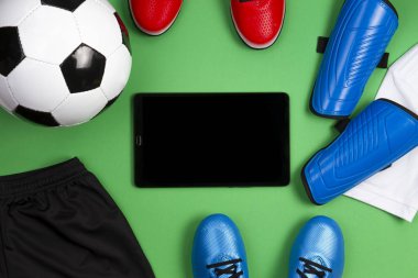 Futbol futbol arka plan. Futbol topu, mavi çizmeler, ayakkabısı, Beyaz tişört ve yeşil zemin üzerine siyah şort ile tablet bilgisayar. Üstten Görünüm