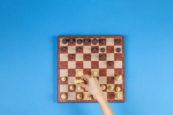 Kid hands over a chessboard playing chess game on blue background, top view — Stock Photo, Image