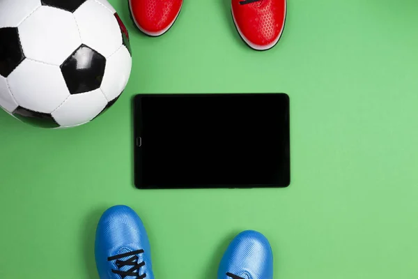 Soccer football background. Top view of two soccer players shoes, soccer ball and tablet computer on green background