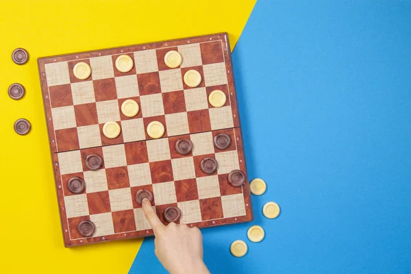 Child hands playing checkers on checker board game over yellow and blue background, top view — Stock Photo, Image