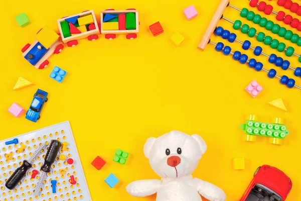 Kinderspielzeug Hintergrund. Teddybär, Holzeisenbahn, bunte Bauklötze, Spielzeug-Set, Autos, Abakus auf gelbem Hintergrund — Stockfoto