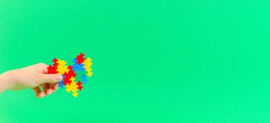 Yeşil arka plan üzerinde renkli kalp tutan çocuk el. Dünya otizm farkındalık günü kavramı