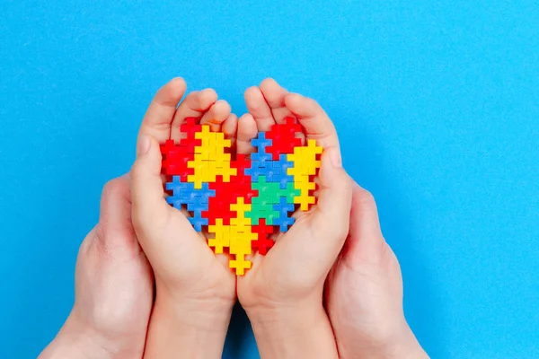 Mani per adulti e bambini che tengono il cuore colorato su sfondo blu. World autism awareness day concept — Foto Stock