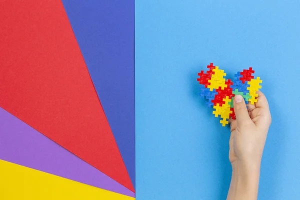 Bambino mano tenendo cuore colorato su sfondo multicolore. World autism awareness day concept — Foto Stock