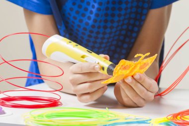 Çocuk el ile 3D yazdırma kalem, beyaz masa üzerinde renkli filamentler oluşturma.