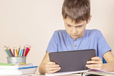 Kitap defterleri ile masada oturan ve tablet bilgisayar kullanan çocuk