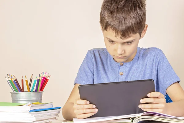 Criança sentada à mesa com cadernos de livros e usando computador tablet — Fotografia de Stock