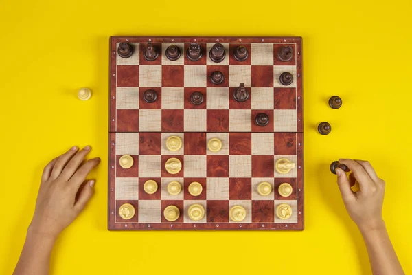 Kid hands over a chessboard playing chess game on yellow background, top view — Stock Photo, Image