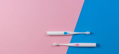 Mavi ve pembe arka planda iki diş fırçası. Üst görünüm