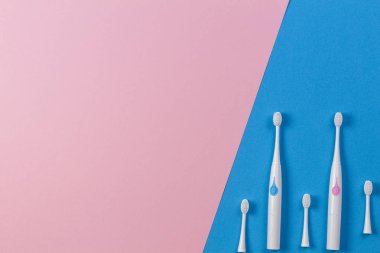 Mavi ve pembe arka planda üç fırça başlı iki elektrikli diş fırçası. Üstte görüntü