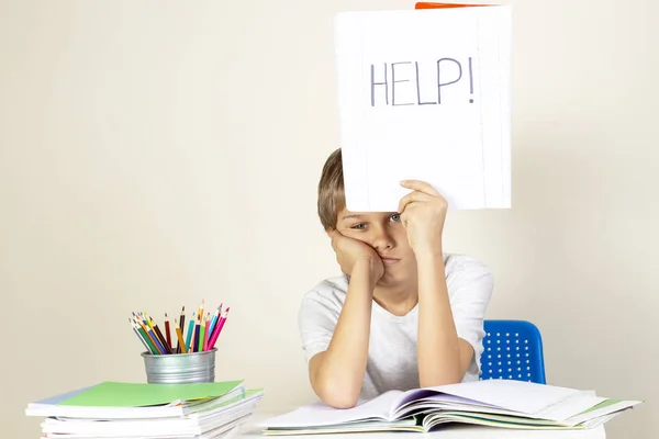 Aide à signer. Triste fatigué malheureux enfant faire ses devoirs et tenant un carnet avec mot Aide — Photo