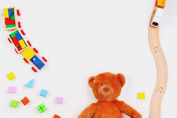 Dětské hračky pozadí. Medvídek, dřevěný vlak, barevné cihly na bílém stole — Stock fotografie