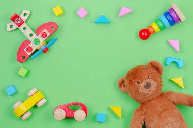 Oyuncak ayı, ahşap uçak, arabalar, bebek istifleme halkaları piramit ve yeşil arka plan üzerinde renkli bloklar ile Çocuk oyuncakları arka plan çerçevesi