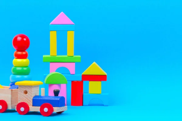 Παιδικό παιχνίδι. Ξύλινο παιχνίδι τρένο, μωρό στοίβα δαχτυλίδια πυραμίδα και πολύχρωμα τουβλάκια σε μπλε φόντο — Φωτογραφία Αρχείου
