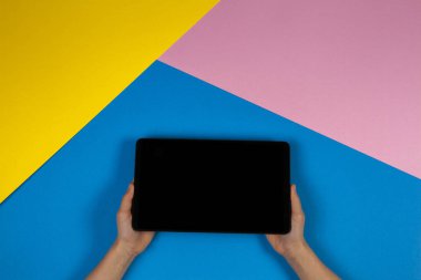 Mavi pembe ve sarı arka planda tablet bilgisayar ile çocuk elleri, üst görünüm