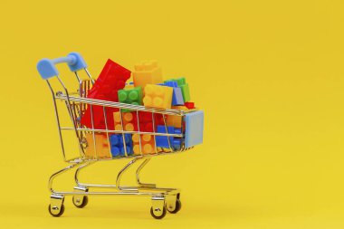Sarı arka planda renkli tuğlalarla dolu alışveriş arabası arabası