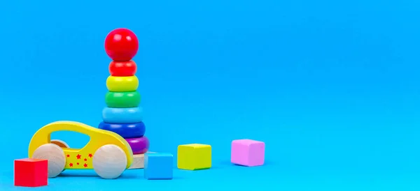 Дитячий іграшковий фон. Дерев'яний іграшковий потяг, дитячі кільця для укладання піраміди та барвисті блоки на синьому фоні — стокове фото