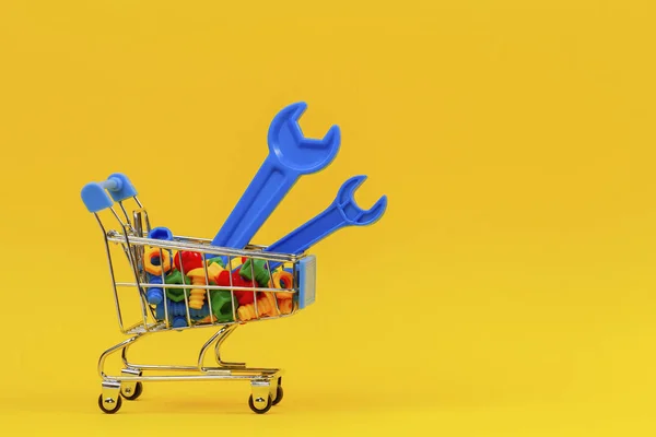 Panier chariot d'achat avec des outils de clés bleues et plein de boulons colorés sur fond jaune — Photo