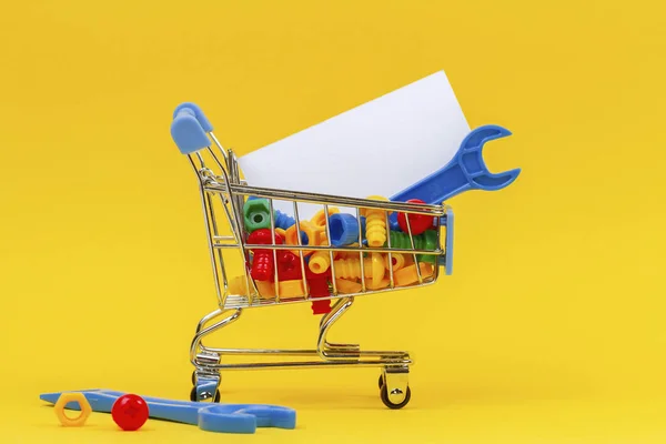 Panier chariot d'achat avec des outils de clés bleues et plein de boulons colorés sur fond jaune — Photo