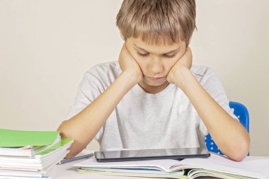 Kitap defterleri ile masada oturan ve tablet bilgisayar kullanan çocuk