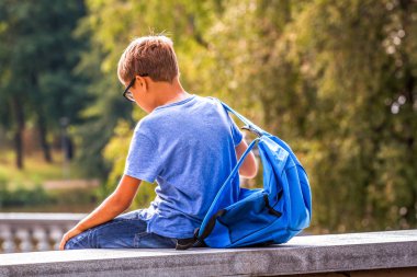 Okuldan sonra açık havada oturan sırt çantası ile yorgun çocuk