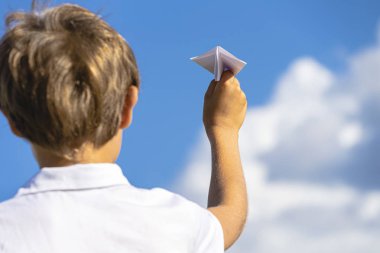Mavi gökyüzüne karşı beyaz kağıt uçağı ile çocuk el