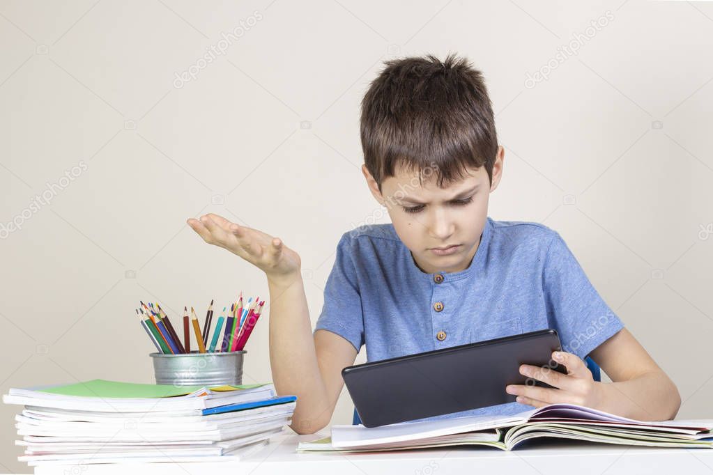 Confused,surprised child with tablet computer sitting at table with books notebooks