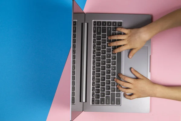 Kid händer att skriva på laptop dator tangentbord, ovanifrån, rosa och blå bakgrund — Stockfoto