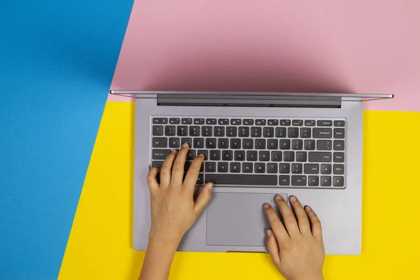 Kid händer att skriva på bärbar datortangentbord på blå, gul och rosa bakgrund, uppifrån — Stockfoto