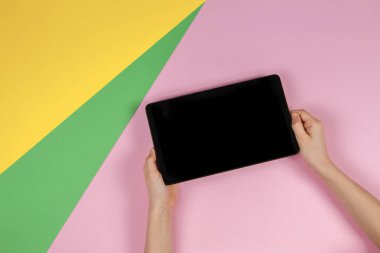 Pastel pembe, sarı ve açık yeşil arka plan üzerinde tablet bilgisayar ile Çocuk eller. Üstte görüntü