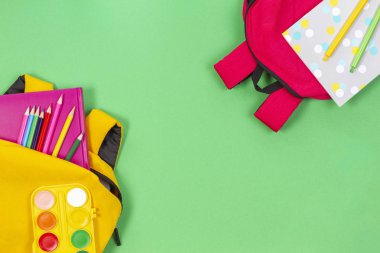 Okul konseptine geri dönelim. Açık yeşil arka plan üzerinde okul malzemeleri, kitap ve defterler ile sarı ve pembe sırt çantaları. Üstte görüntü