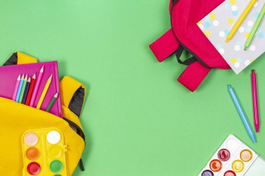 Okul konseptine geri dönelim. Açık yeşil arka plan üzerinde okul malzemeleri, kitap ve defterler ile sarı ve pembe sırt çantaları. Üstte görüntü