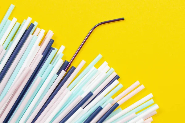 Stainless steel reusable drinking straw with many multicolored plastic straws on yellow background