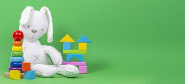 Beyaz peluş oyuncak tavşan, bebek istifleme halkaları piramit ve açık yeşil arka plan üzerinde renkli ahşap bloklar