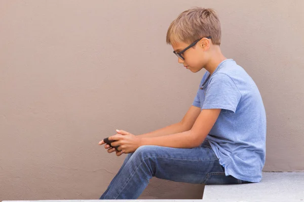 Menino sentado com telefone celular e jogar jogos online ao ar livre — Fotografia de Stock