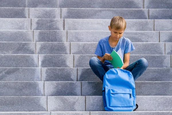 Pojke som läser boken sitter på trappan utomhus — Stockfoto